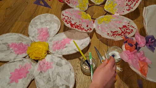 A selection of in-progress blossom lanterns on the floor, with a hand adding decorations.